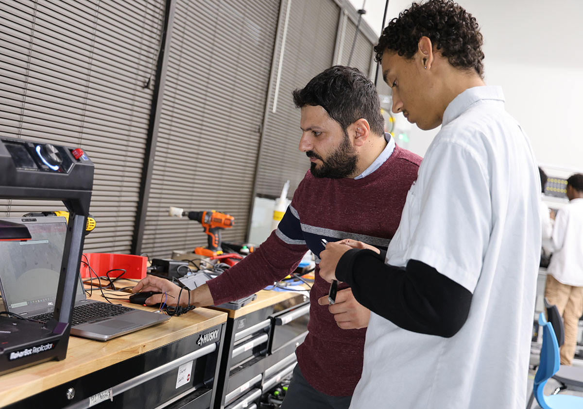 HSA Teacher smiles while kneeling beside a young student in a classroom setting.